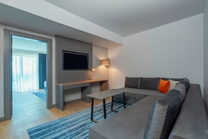 Een moderne woonkamer met een grijze bank, een flatscreen televisie aan de muur, een bijzettafeltje en een vloerlamp.