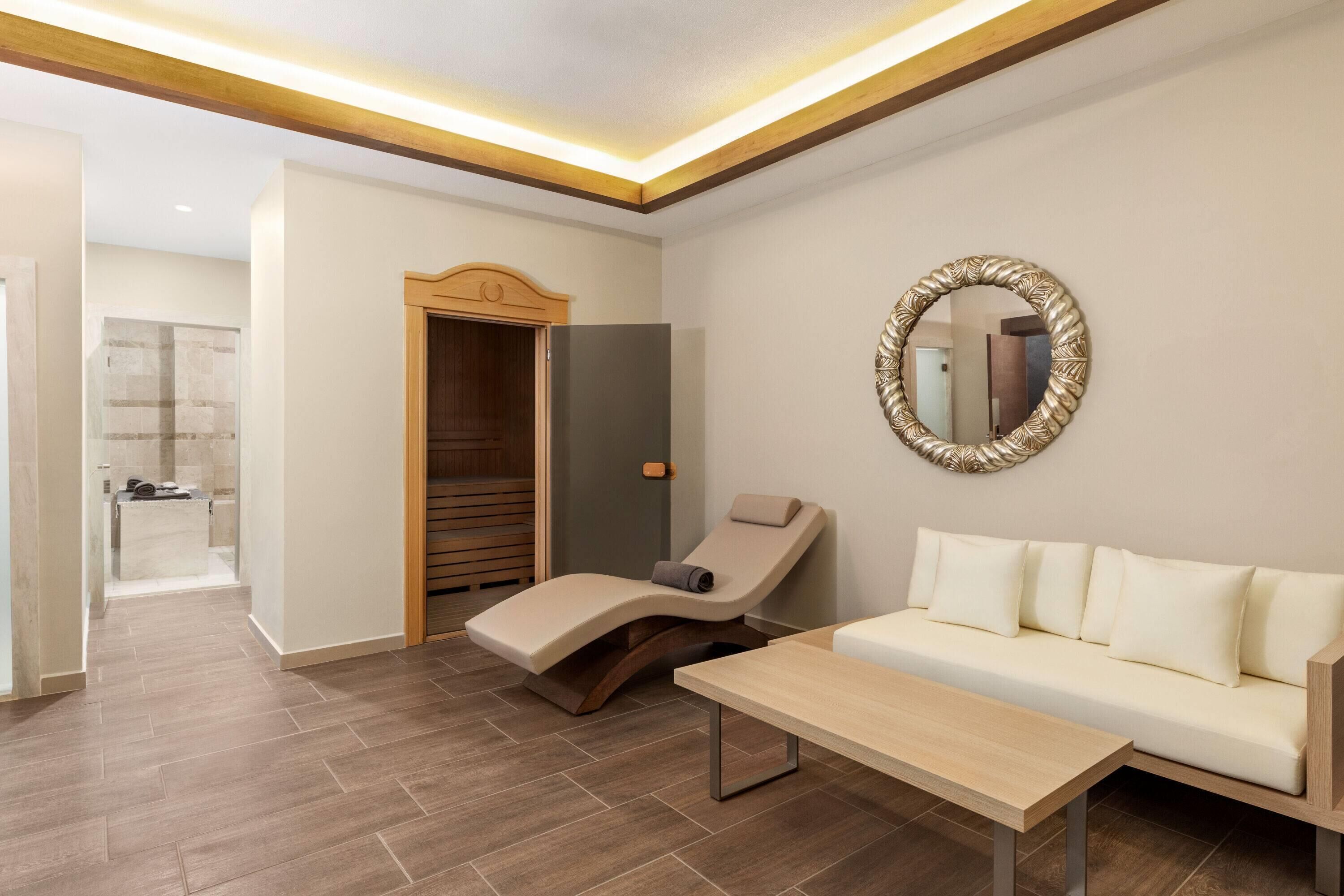 A modern spa room with a massage table, a sofa, and a mirror.