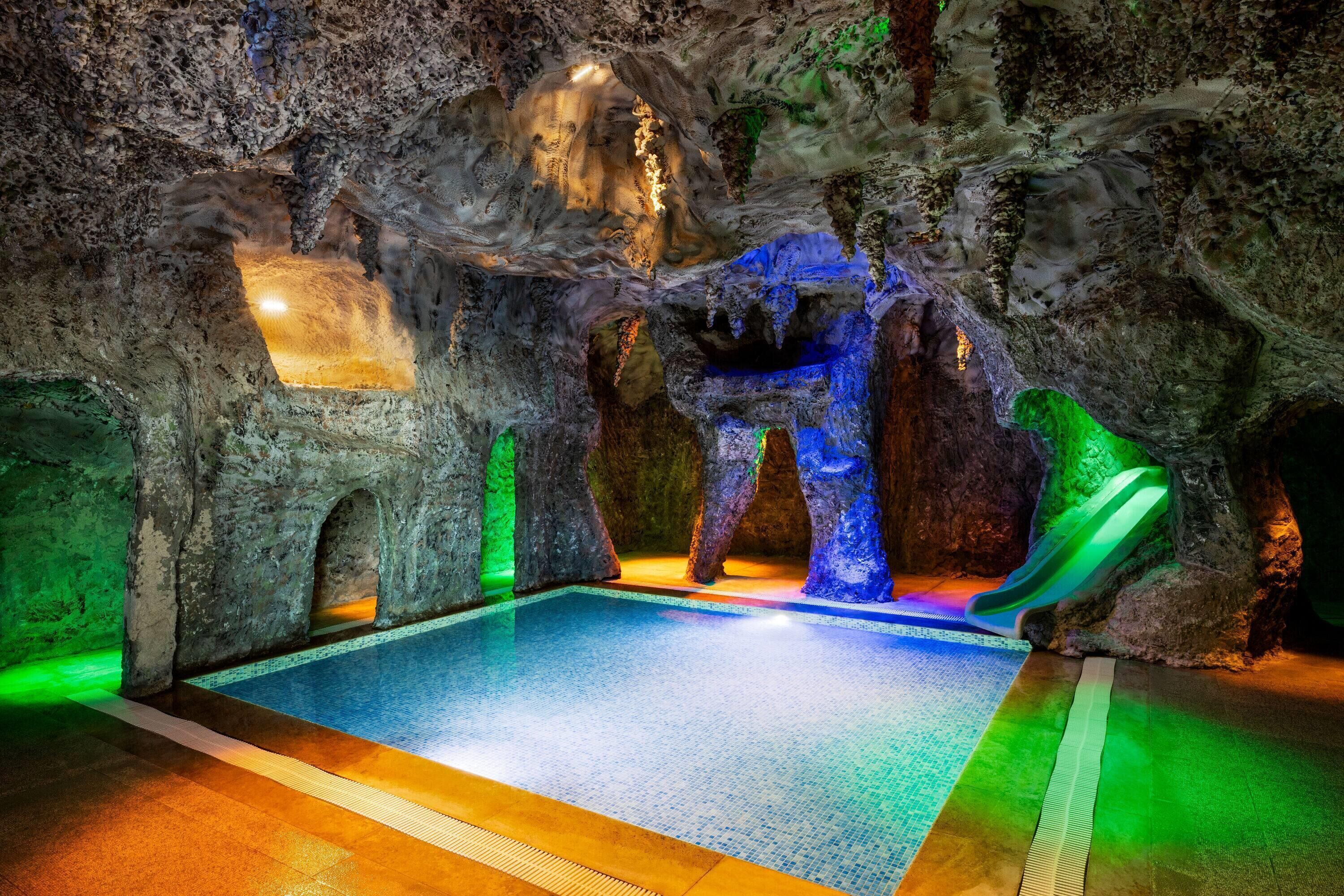 An indoor pool with a rocky cave-like environment, illuminated by colored lights.