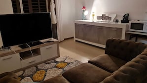 A living room with a flat-screen TV, a sofa, a coffee table, and a kitchen area with a microwave and a cabinet. - T4 5 min from the beach (schoelcher)