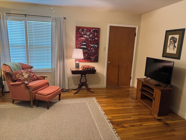A living room with a wooden floor, a red armchair, a television, and a door. - Spacious 3 bedroom, 1.5 bath House. Wi-Fi, Roku TV, Fully stocked kitchen, etc! (Lampasas)