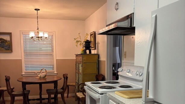 A kitchen with a stove, refrigerator, dining table, chairs, and a chandelier.