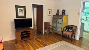 A living room with a wooden entertainment unit, a flat-screen TV, a wicker chair, a patterned rug, and a cabinet with decorative items.