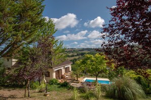 A house with a swimming pool, surrounded by trees and a view of the countryside.