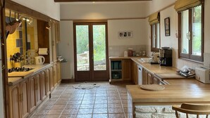 A spacious kitchen with wooden cabinets, a stone backsplash, and a large island with bar stools. - Dordogne gite, amazing views, private heated pool, large gardens, NO ADDED COSTS (Marnac)