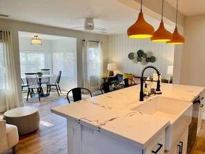 Een moderne keuken met een groot eiland, hanglampen en een eethoek met een tafel en stoelen.