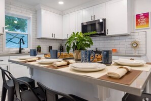 Una cocina moderna con armarios blancos, microondas, ventana grande y una planta.