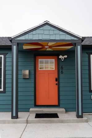Una casa color turquesa con una puerta roja, un buzón y un pequeño porche con un toldo decorativo.