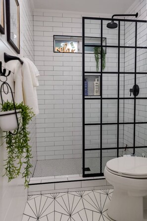 A bathroom with white subway tiles, a black shower enclosure, a toilet, and a hanging plant.