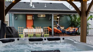 A hot tub with a wooden pergola overhead, a dining table with chairs, and a hammock outside a house. - Rise & Grind SLC HIGH-END Style/Gated n Garage-2Br (South Salt Lake)