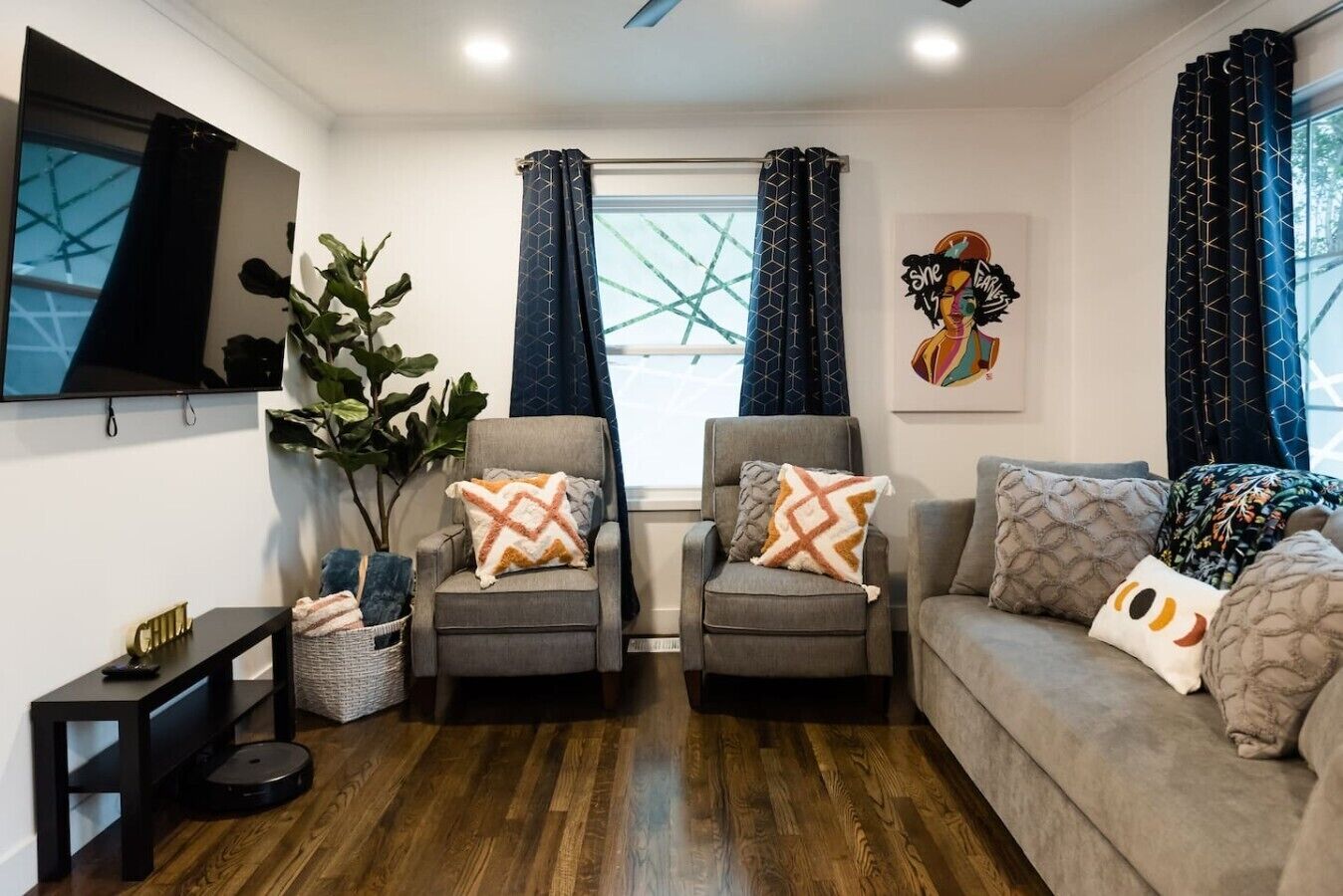 A living room with two armchairs, a sofa, a TV, a large window with curtains, and a plant.
