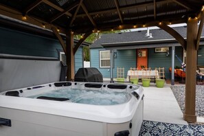 Un jacuzzi bajo un porche cubierto, con una casa al fondo.