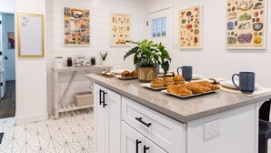 A modern kitchen with white cabinetry, a central island with baked goods, and educational posters on the walls. - Rise & Grind SLC HIGH-END Style/Gated n Garage-2Br (South Salt Lake)