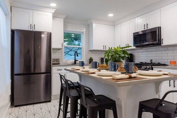A modern kitchen with white cabinets, stainless steel appliances, a central island with bar stools, and a large window.