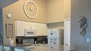 A kitchen with a central island, white cabinets, a microwave, and a refrigerator. There are three bar stools and a clock on the wall.