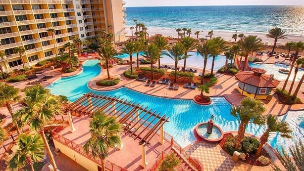 A resort with a large pool area, palm trees, and a view of the ocean.