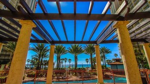 A covered outdoor area with a pool, palm trees, and a view of the ocean.