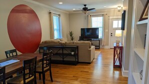A living room with a wooden floor, a large red exercise ball, a sofa, a TV, and a dining area with a table and chairs. - Casa Rosa - 2BR West End Bungalow (Durham)