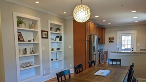 A dining area with a wooden table and chairs, surrounded by white shelving units with decorative items. - Casa Rosa - 2BR West End Bungalow (Durham)