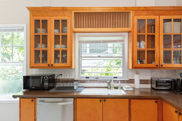 A kitchen with wooden cabinets, a microwave, a toaster, and a window with a view of greenery.