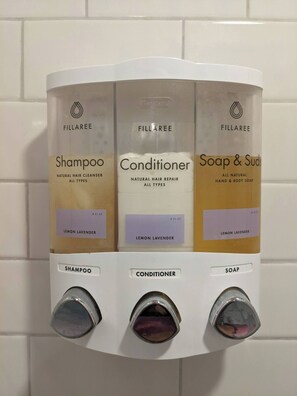 A wall-mounted dispenser with three compartments for shampoo, conditioner, and soap & suds, each labeled with the brand Fillaree and a lemon lavender scent.