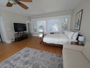 A bedroom with a bed, a TV, a ceiling fan, and a window with blinds.