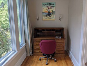 A room with a wooden desk, a purple chair, a window with curtains, and a poster on the wall.