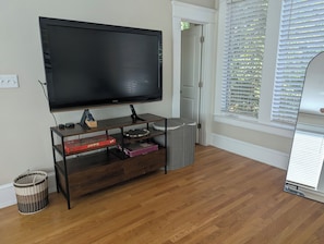 A living room with a flat-screen TV on a wooden stand, a wicker basket, and a trash can.