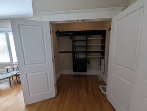 A walk-in closet with a black hanging rod and shelves, wooden flooring, and a white door. - The Trinity Garden Suite, King Bed Near Duke (Durham)