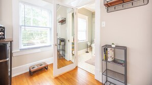 A room with a wooden floor, a metal bookshelf, a mirror, and a window with blinds.