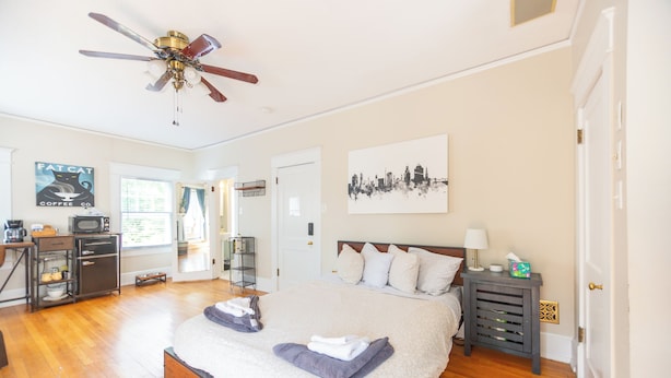 A spacious bedroom with a large bed, a ceiling fan, a cityscape artwork, and a coffee station.
