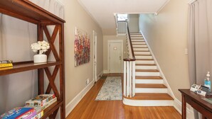 A hallway with wooden flooring, a white staircase, a bookshelf with books, and a painting on the wall.