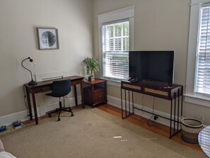 Cozy retreat with a comfortable bed, desk for work, and a TV for entertainment, offering a peaceful view of the outdoors.