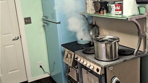 Une cuisine avec un four ancien, un réfrigérateur bleu et une étagère remplie d’ustensiles de cuisine.