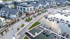 Un moderno paseo marítimo urbano con edificios contemporáneos, un puerto deportivo con barcos y una zona peatonal.