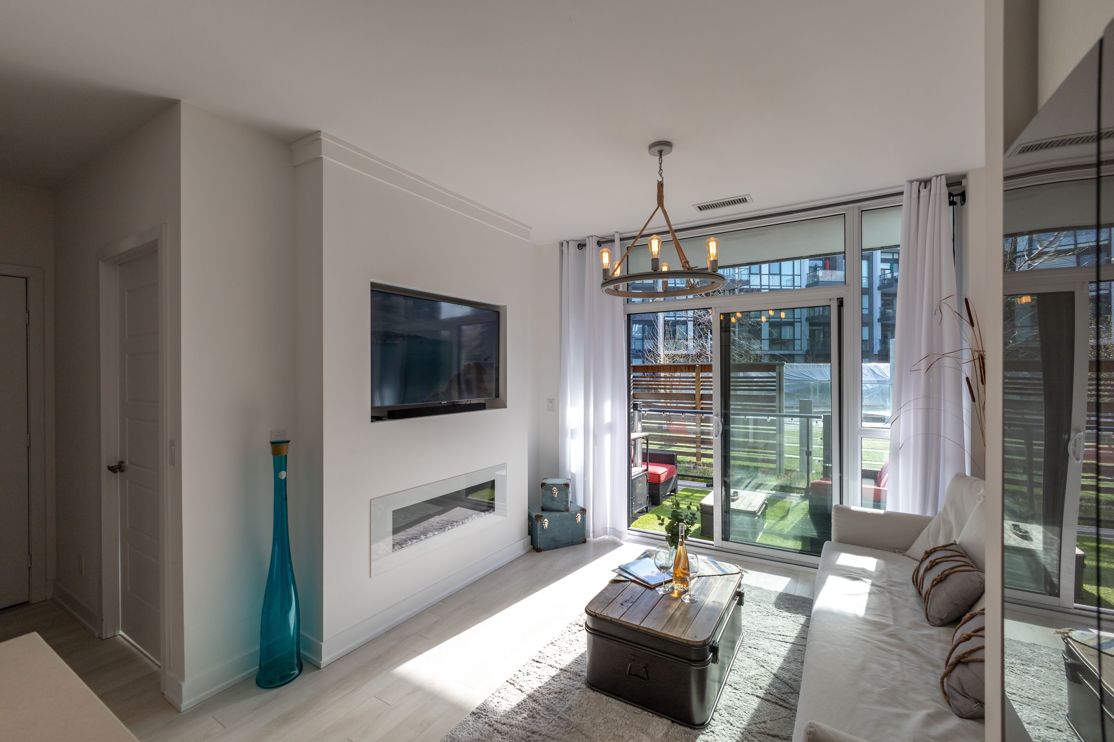 A modern living room with a large TV, a fireplace, a sofa, and a view of the outdoors.