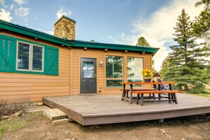 Una cabaña de madera con terraza, chimenea y una puerta con contraventanas verdes.