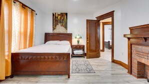 A bedroom with a wooden bed, a nightstand, a lamp, a patterned rug, and a fireplace. - Buffalo Vacation Rental ~ 20 Mi to Niagara Falls! (Buffalo)