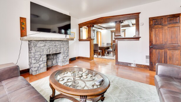 A living room with a stone fireplace, a flat-screen TV, leather sofas, and a dining area visible through an archway. - Buffalo Vacation Rental ~ 20 Mi to Niagara Falls! (Buffalo)