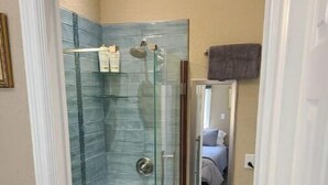 A narrow bathroom with a glass shower enclosure, a vanity with cabinets, and a mirror. - Tropical Paradise studio #3 (Tampa)