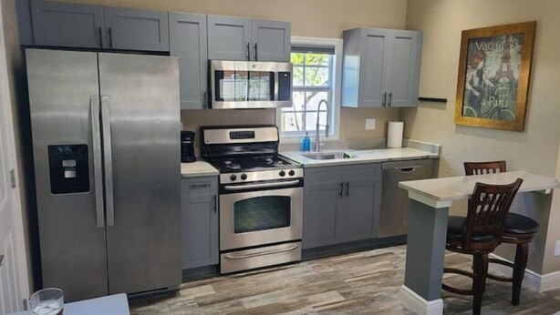 A modern kitchen with grey cabinets, stainless steel appliances, and a dining area with a table and chairs. - Tropical Paradise studio #3 (Tampa)