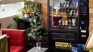 Ein Zimmer mit einem Getränkeautomaten, einem roten Sessel, einem kleinen Tisch mit einem Glas und einem Weihnachtsbaum.