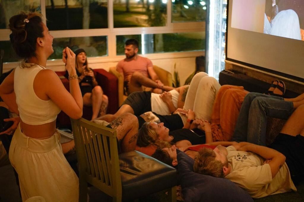 Um grupo de pessoas reunido em volta de uma televisão num quarto com uma janela grande.