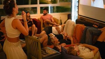 Um grupo de pessoas reunido em volta de uma televisão num quarto com uma janela grande.