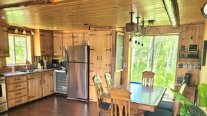 Una cocina tipo cabaña de madera con un refrigerador de acero inoxidable, armarios de madera y una mesa de comedor con sillas.