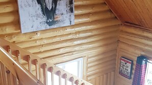 Un interior de madera con una escalera de madera, una obra de arte con un cráneo de toro en la pared y una ventana con cortinas a cuadros.