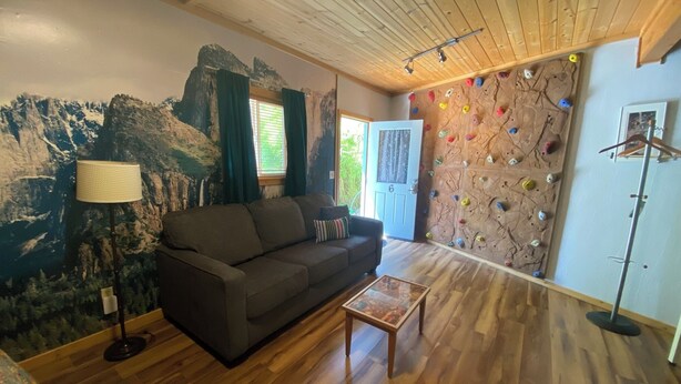 A living room with a wooden ceiling, a sofa, a coffee table, a climbing wall, and a door leading outside. - The Rock Climbing Suite (Nevada city)