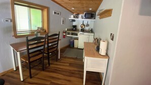 A compact kitchen with wooden flooring, a dining table with chairs, a window with blinds, and basic kitchen appliances. - The Rock Climbing Suite (Nevada city)