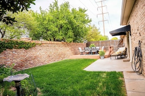 Ein Garten mit einer Backsteinmauer, einem Rasen, einer Terrasse mit Gartenmöbeln und einem an der Mauer aufgerollten Gartenschlauch.
