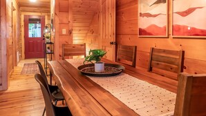 A wooden interior with a dining table, chairs, a chandelier, and artwork on the walls. - 6BR Log Cabin | Walk to Downtown | Mountain Views (West Jefferson)